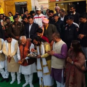 Group of men in traditional Indian attire praying during a ceremonial ritual, with a priest holding a plate of offerings.